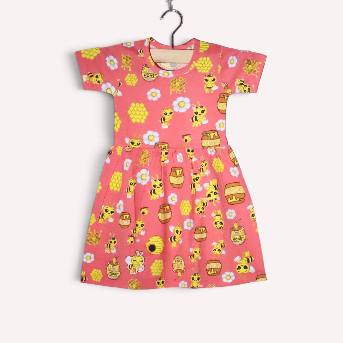 Bright peach baby frock with an allover bee, honeycomb and honey jar print, accented with white flowers, featuring short sleeves and a gathered waist