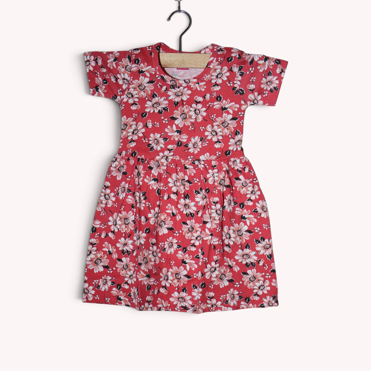 Coral red cotton baby frock featuring white, light pink and black flowers, with short sleeves, a round neckline and a gathered waist.