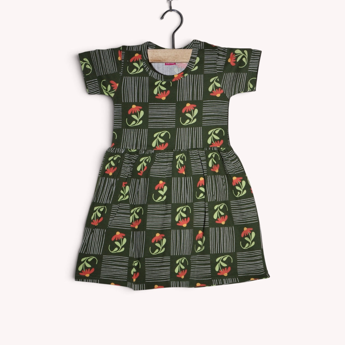 Dark green cotton baby frock featuring coral flowers, light green leaves and white stripes arranged in a geometric pattern, with short sleeves and a gathered waist.