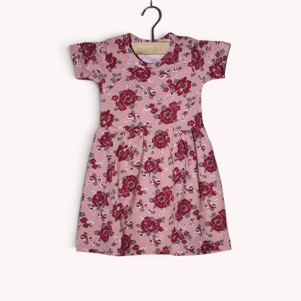 Dusty pink baby frock with an allover floral print in burgundy, maroon, white and grey, featuring short sleeves and a gathered waist