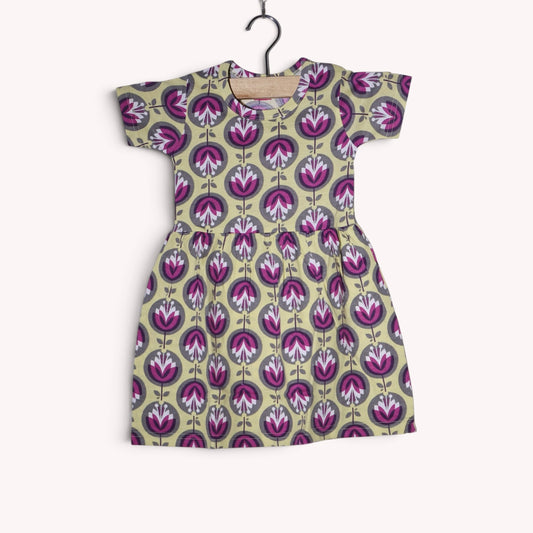 Dusty beige baby frock with a repeating stylised floral print in purple, magenta, white and grey, featuring short sleeves and a gathered waist