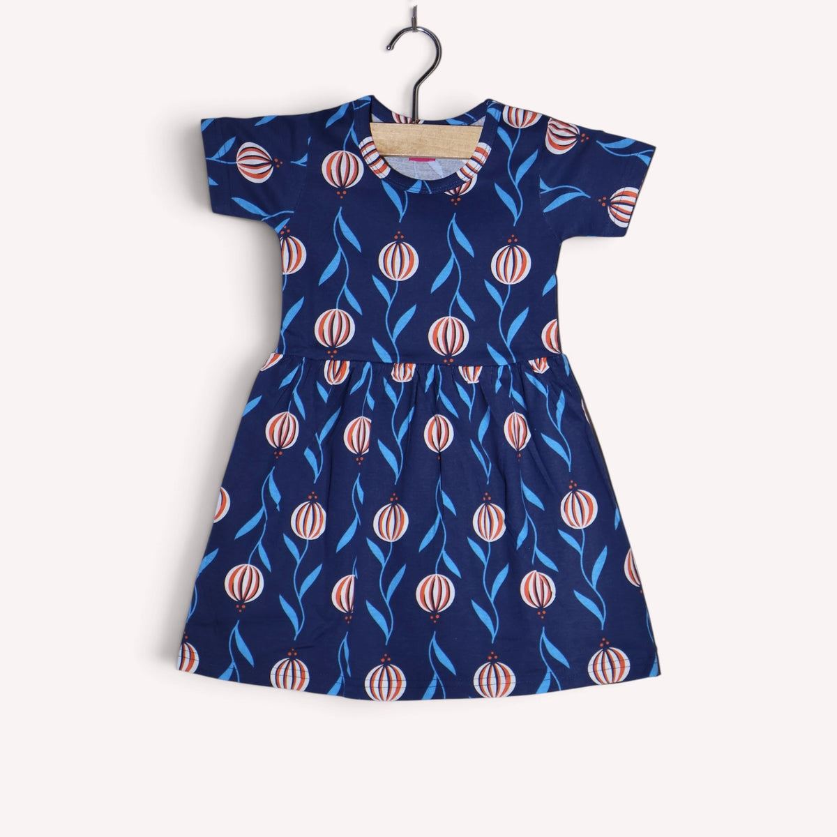 Navy blue cotton baby frock featuring a lantern print with blue leaves and white and orange striped details, short sleeves and a gathered waist.