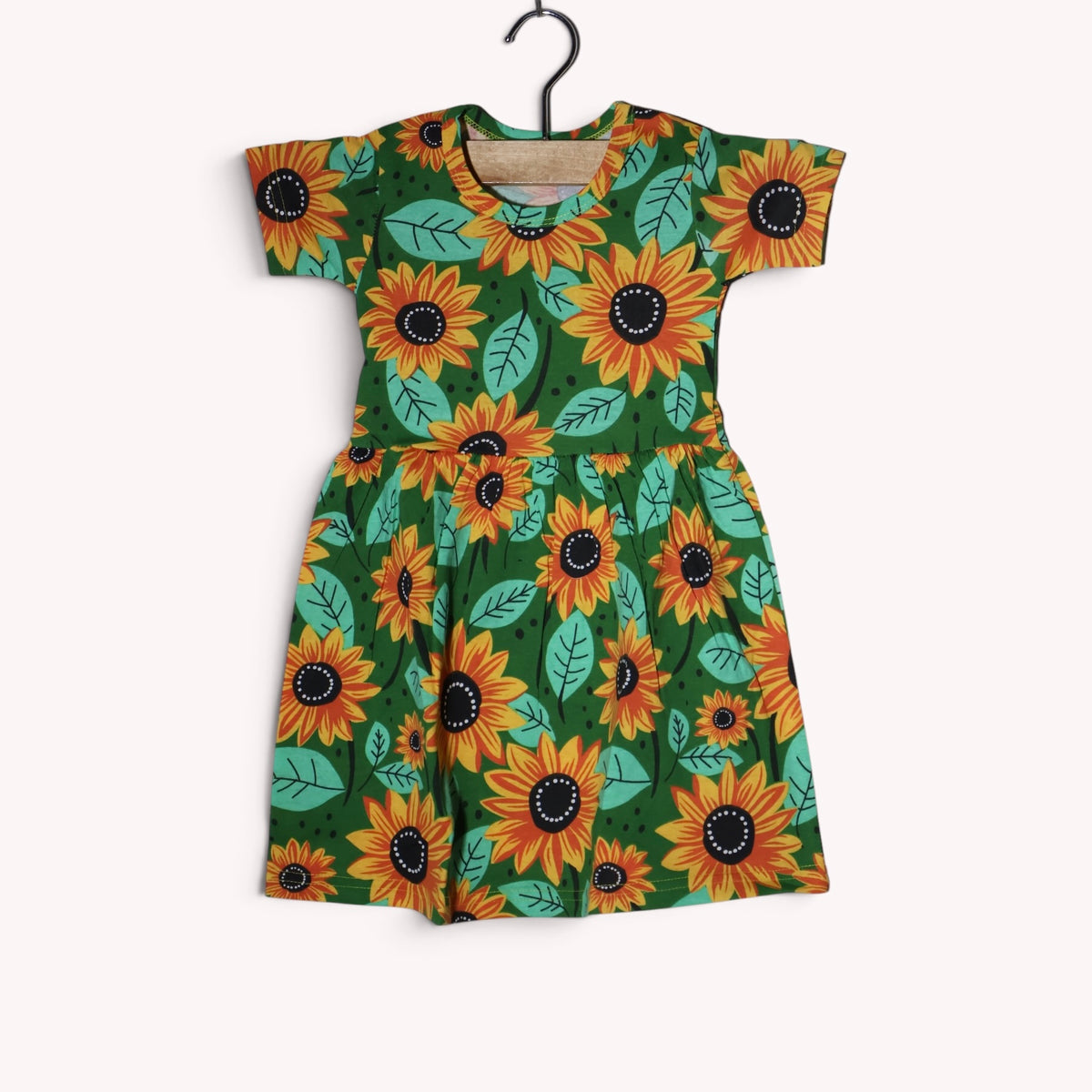 Dark green baby frock with an allover sunflower print in yellow, orange and black, with mint-green leaves, short sleeves and a gathered waist