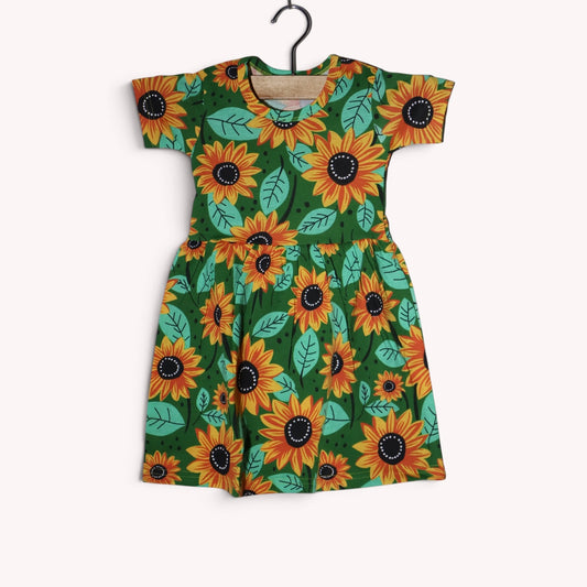Dark green baby frock with an allover sunflower print in yellow, orange and black, with mint-green leaves, short sleeves and a gathered waist